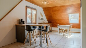 Een eetruimte met een houten plafond, een keukentafel, barstoelen, een eettafel met stoelen en een raam.