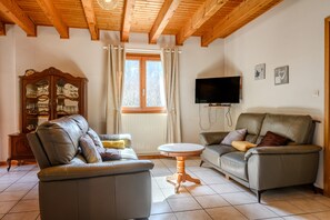 Ein Wohnzimmer mit zwei Sofas, einem Holzschrank, einem Fernseher und einem Fenster mit Vorhängen.