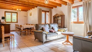Een gezellige woonkamer met een bank, stoelen, een eettafel en een houten plafond.