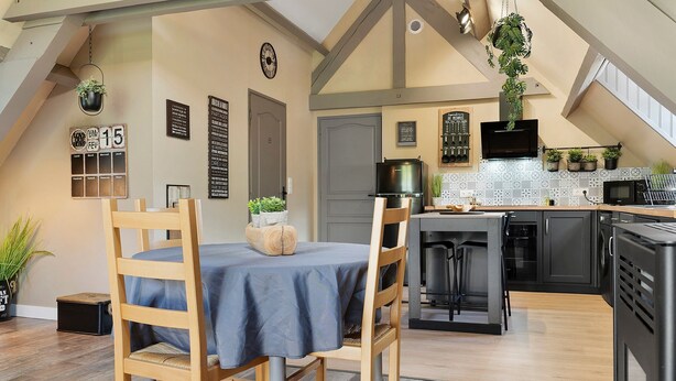 Un comedor con mesa y sillas, una cocina equipada y un dormitorio en entrepiso con cama.