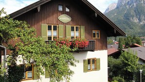A traditional wooden building with a sign reading "Landhaus Albrecht." It features multiple windows with shutters, a balcony with flowers, and a mountainous backdrop. - Landhaus Albrecht - Holiday apartment 02 (51 m²) for 2 guests with large balcony (Mittenwald)