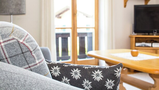 A living room with a sofa, a table, a television, and a window with a view of the outside. - Landhaus Albrecht - Holiday apartment 02 (51 m²) for 2 guests with large balcony (Mittenwald)