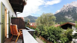 A wooden deck with a bench and a table, surrounded by greenery and a wooden fence, overlooking a mountainous landscape. - Landhaus Albrecht - Holiday apartment 02 (51 m²) for 2 guests with large balcony (Mittenwald)