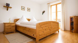 A bedroom with a wooden bed, a nightstand, a bedside table, a window with curtains, and a bookshelf. - Landhaus Albrecht - Holiday apartment 02 (51 m²) for 2 guests with large balcony (Mittenwald)