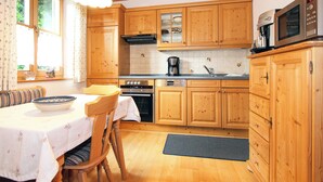 A kitchen with wooden cabinets, a stove, a microwave, and a dining area with a table and chairs. - Landhaus Albrecht - Holiday apartment 02 (51 m²) for 2 guests with large balcony (Mittenwald)