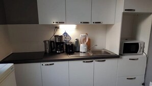 Una cocina moderna con gabinetes blancos, encimera negra y varios electrodomésticos, como una cafetera, tostadora y microondas.