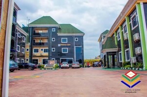 Um hotel com vários andares, teto verde, várias varandas e um estacionamento com carros.