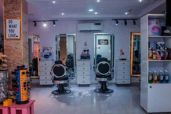 A salon with three chairs, a mirror, and shelves with hair products. - D&G Hotels & Suites (Lagos)