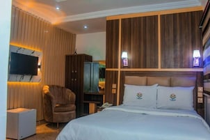 Quarto de hotel com cama, cadeira, televisão e secretária com candeeiro.