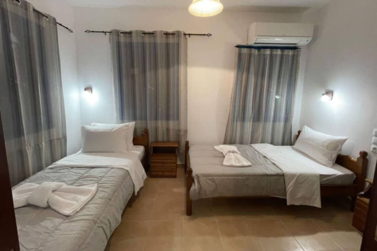 Habitación de hotel con dos camas individuales, una mesita de madera y un ventilador de techo.