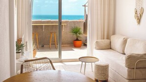 A room with a sofa, a dining table, chairs, a potted plant, a macrame wall hanging, and a view of the sea. - Terraza Azul - Penthouse with sea view by Interhome (Alcocéber/Alcossebre)