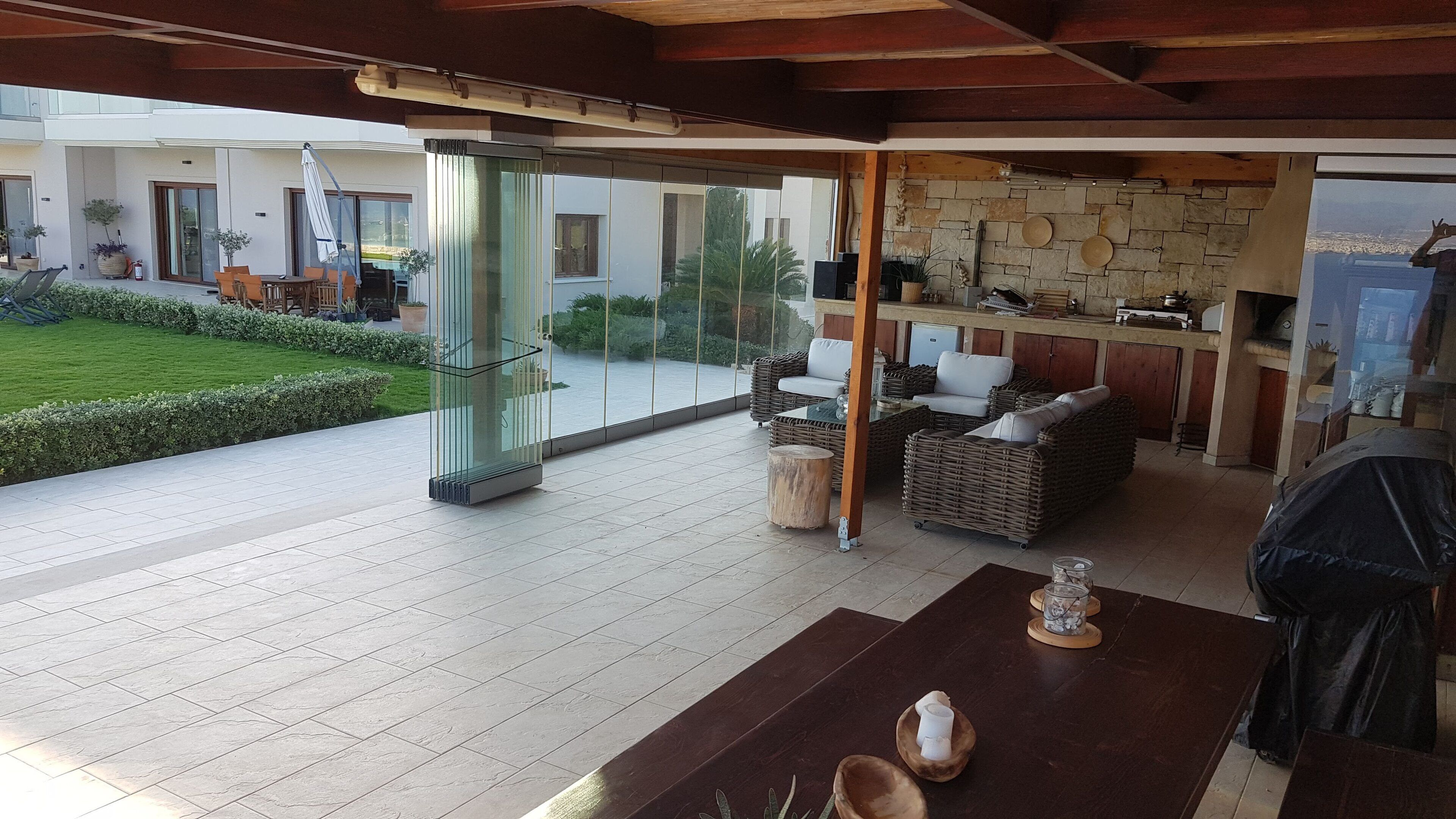 Un vaste espace extérieur doté d’une porte vitrée donnant sur un patio, de meubles en osier et d’un mur en pierre.