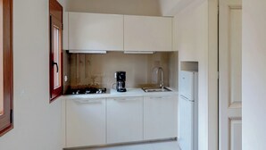 Een compacte keuken met witte kastjes, een koffiezetapparaat, een spoelbak en een koelkast.