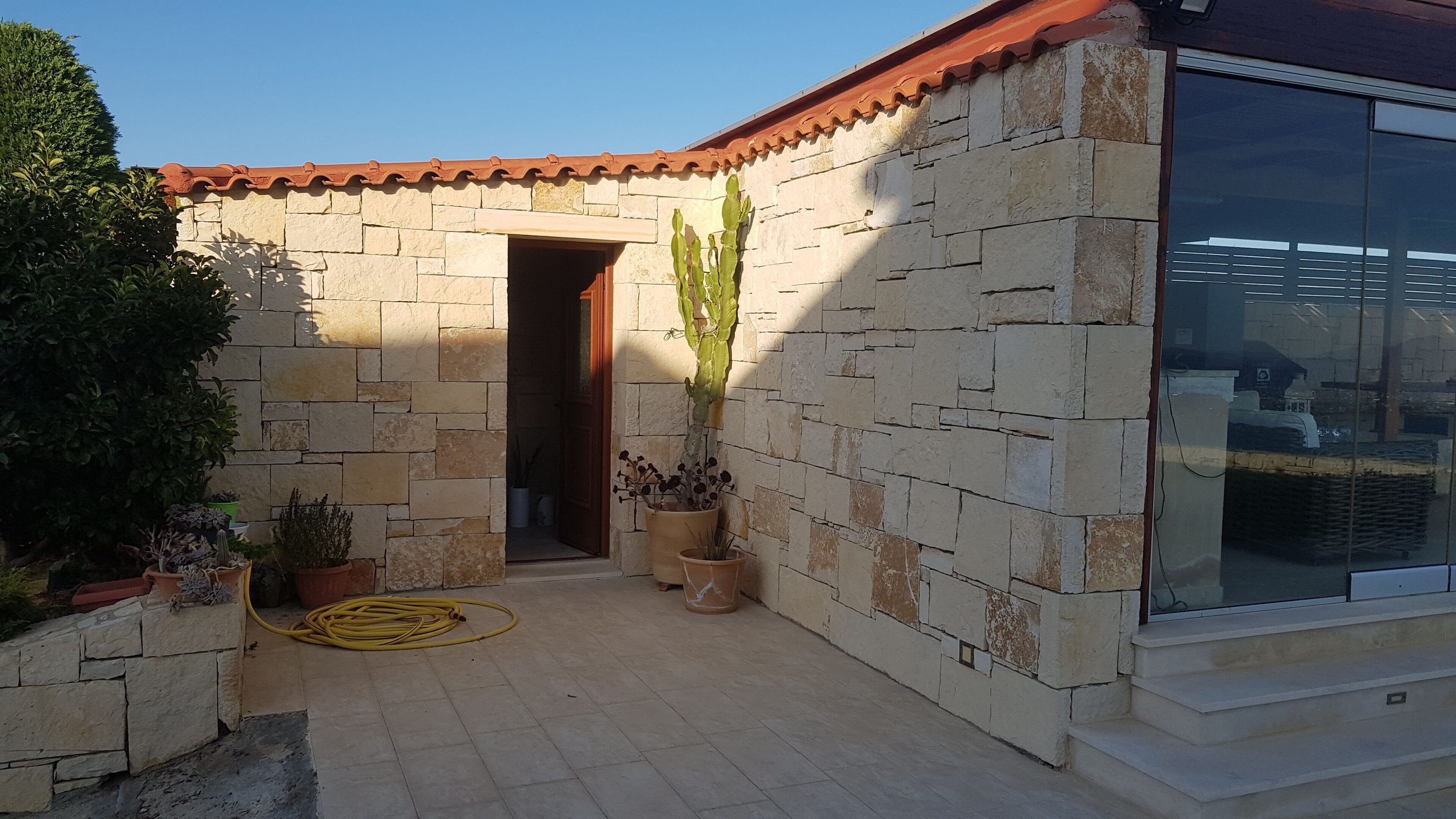 Un bâtiment en pierre avec un toit en tuiles, une grande fenêtre et des plantes en pot.