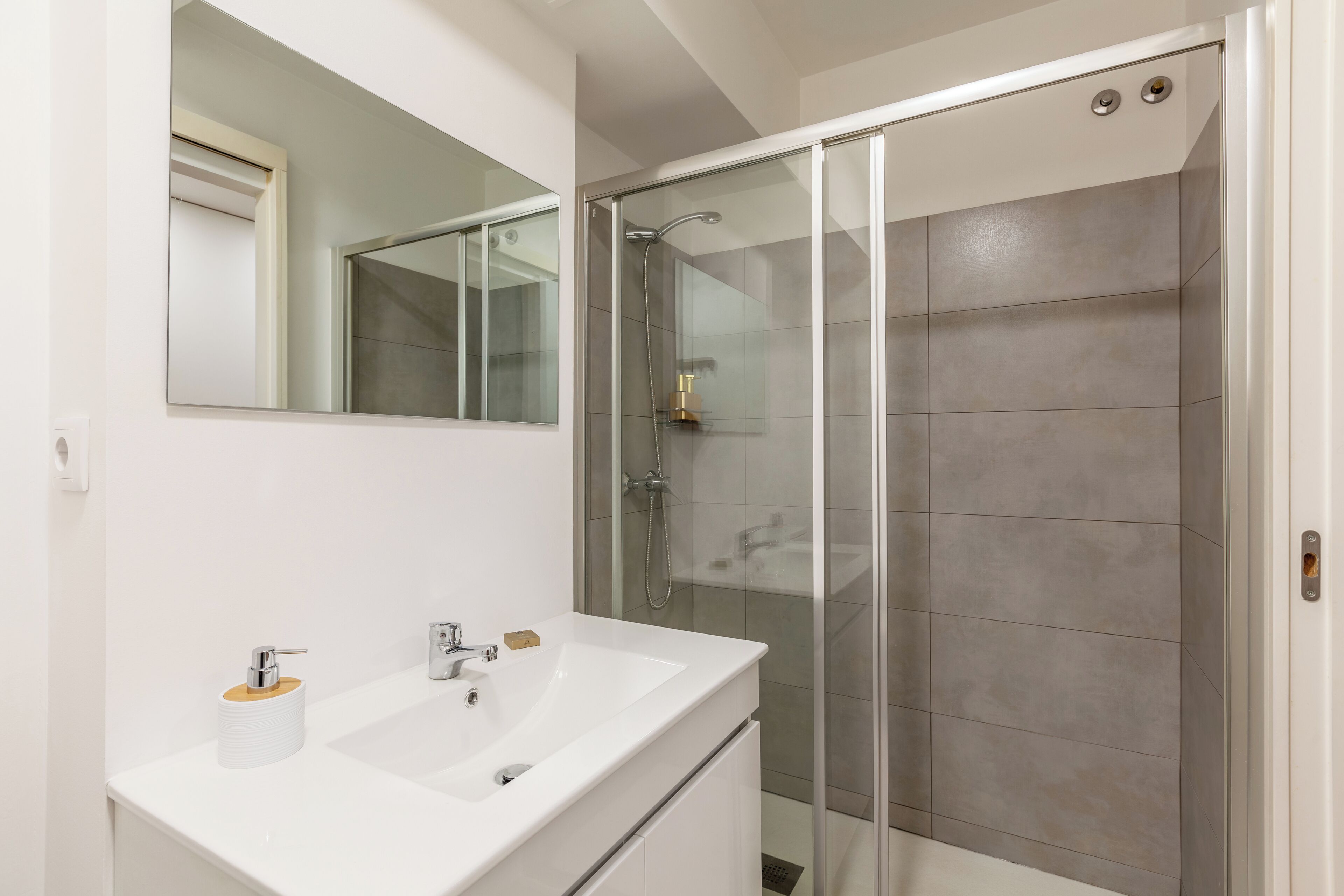 Un baño moderno con un lavabo blanco, un espejo y una ducha con mampara de vidrio.