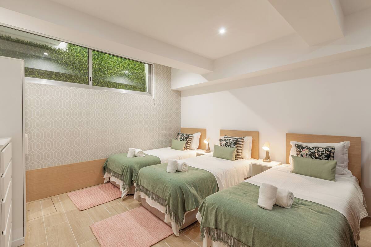 A hotel room with three beds, a window, and a patterned wall.