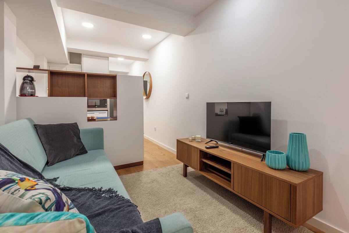 A modern living room with a sofa, TV, wooden entertainment unit, and a kitchen area in the background.
