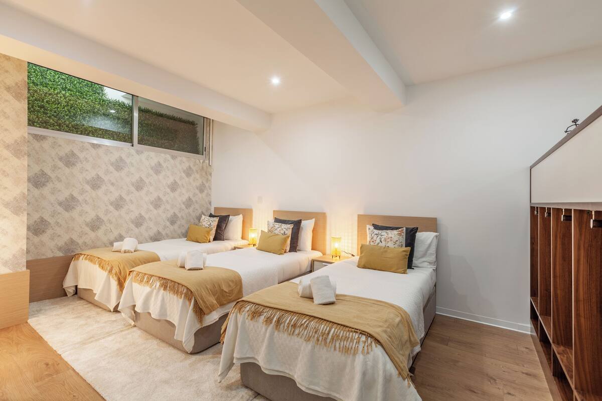 A hotel room with three beds, a large window, and a wooden wardrobe.