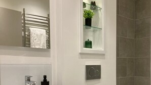 Un baño moderno con un lavamanos blanco, un inodoro y una repisa de vidrio con una planta.
