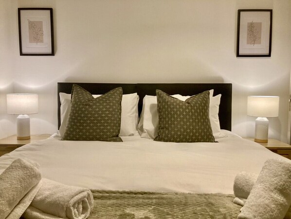 A neatly made bed with a white duvet, two pillows with a geometric pattern, and two plain pillows. There are two bedside lamps on either side of the bed. - Richmond High Street Flat – Station Steps Away (Greater London)