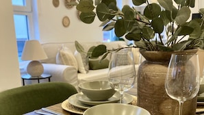 Una mesa de comedor con platos, tazones y cubiertos, un florero con follaje verde, y un recipiente con agua.