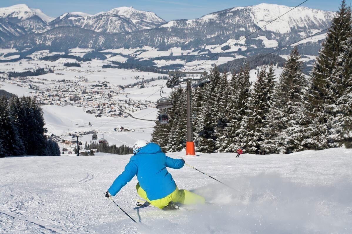 Un paysage de montagne enneigé, avec un télésiège et un skieur au premier plan.