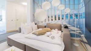 A modern hotel room with a large bed, a sofa, and a view of the sea through floor-to-ceiling windows. - Budapest Downtown Residence LEO (Budapest)