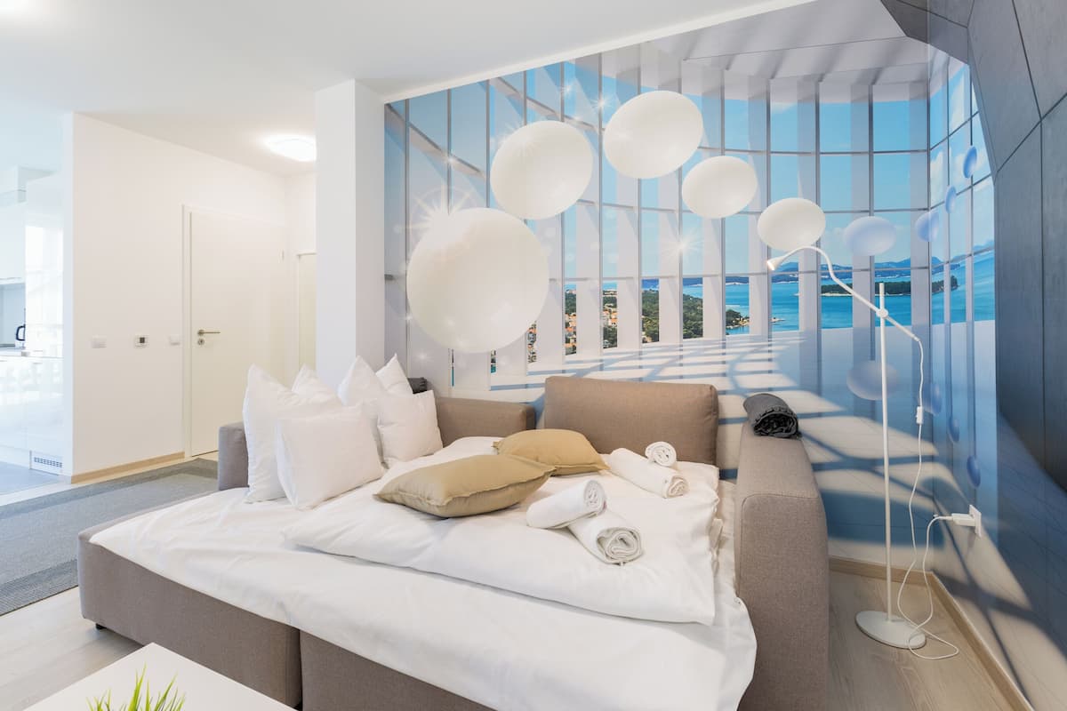 Habitación de hotel moderna con una cama grande, un sofá y vistas al mar a través de ventanales de piso a techo.
