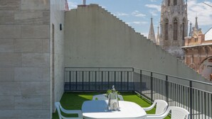 A rooftop terrace with a white table and chairs, a small fountain, and a view of a cathedral. - Budapest Downtown Residence LEO (Budapest)