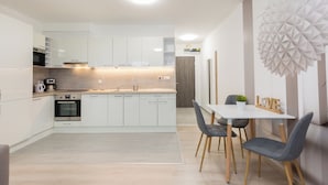 A modern kitchen with white cabinetry, a central island, and a dining area with a white table and gray chairs. - Budapest Downtown Residence LEO (Budapest)