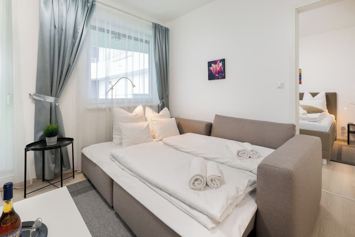 Una habitación de hotel moderna con una cama grande, una mesita con una botella, una planta y un cuadro en la pared.