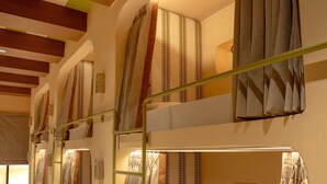 A row of bunk beds with striped curtains, a small shelf with a book, and a wall-mounted light fixture. - Bun And Bunks Udaipur (Udaipur)