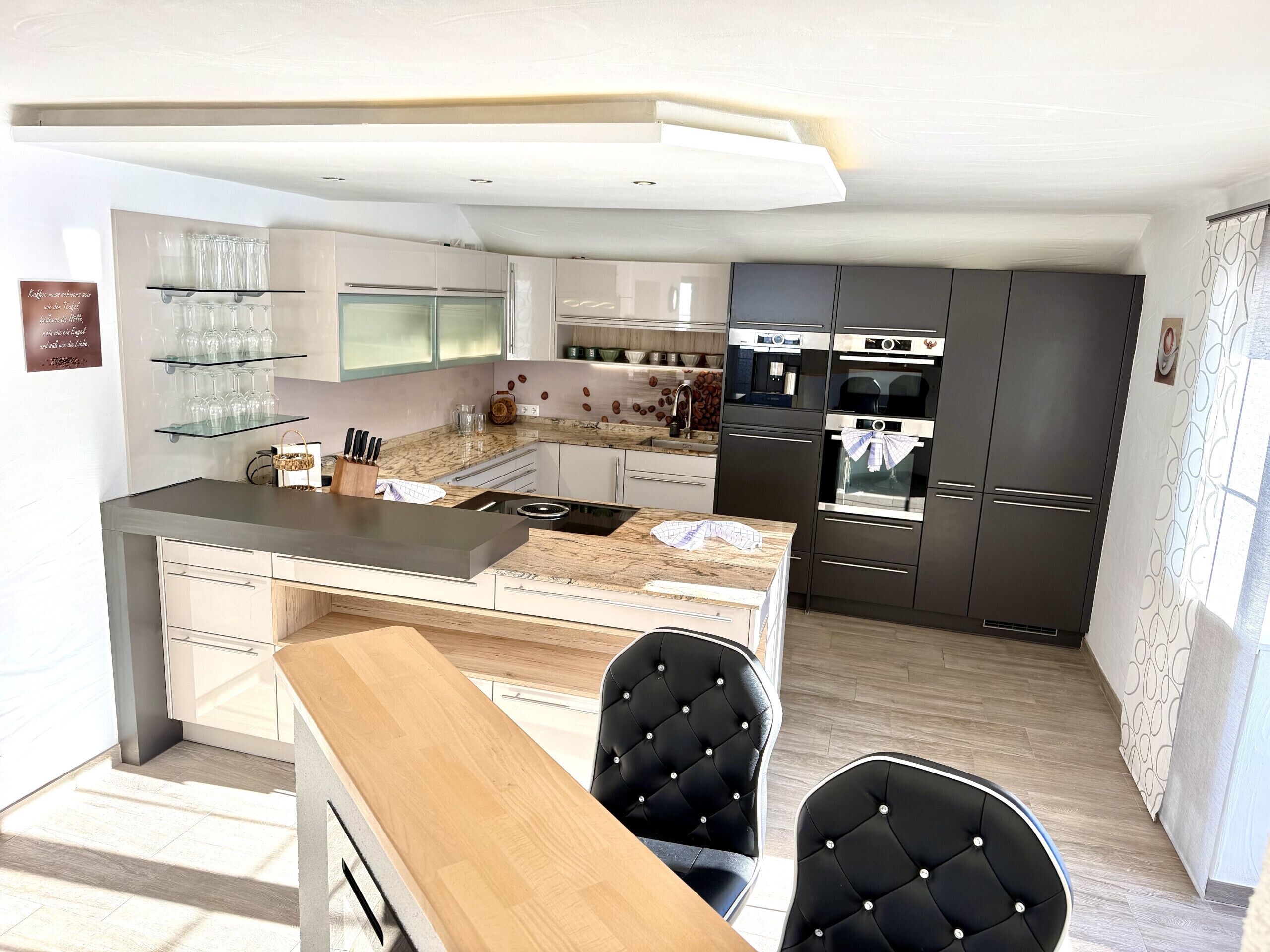 A modern kitchen with a central island, dark cabinets, and a dining area with two chairs.