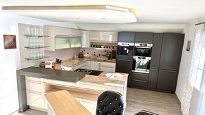 Cozinha moderna com ilha central, armários escuros e área de jantar com duas cadeiras.