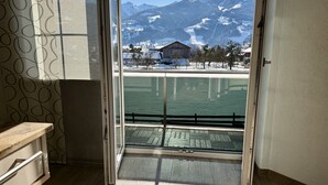 Quarto com uma grande porta de vidro que dá para uma varanda com vista para uma montanha nevada e um corpo de água.