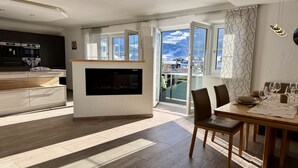Cozinha moderna com forno embutido e micro-ondas, área de jantar com mesa e cadeiras de madeira, e uma grande janela com vista para uma paisagem nevada.