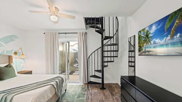 Ein Schlafzimmer mit einem Bett, einem Deckenventilator, einer Treppe, einem Fernseher und einem Bild von einer Strandlandschaft.