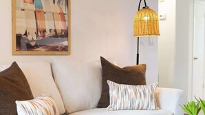 Ein Wohnzimmer mit einer Couch, Kissen, einer Lampe und einem Gemälde von Surfbrettern.