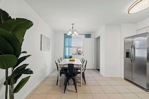 A kitchen with a dining table, chairs, a refrigerator, and a plant.