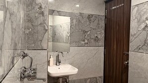 Un bany amb parets de marbre, un lavabo, un mirall i una dutxa.
