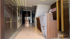 Zona de recepció d'hotel amb taulell de marbre, panells de fusta i senyalitzador d'entrada/sortida.