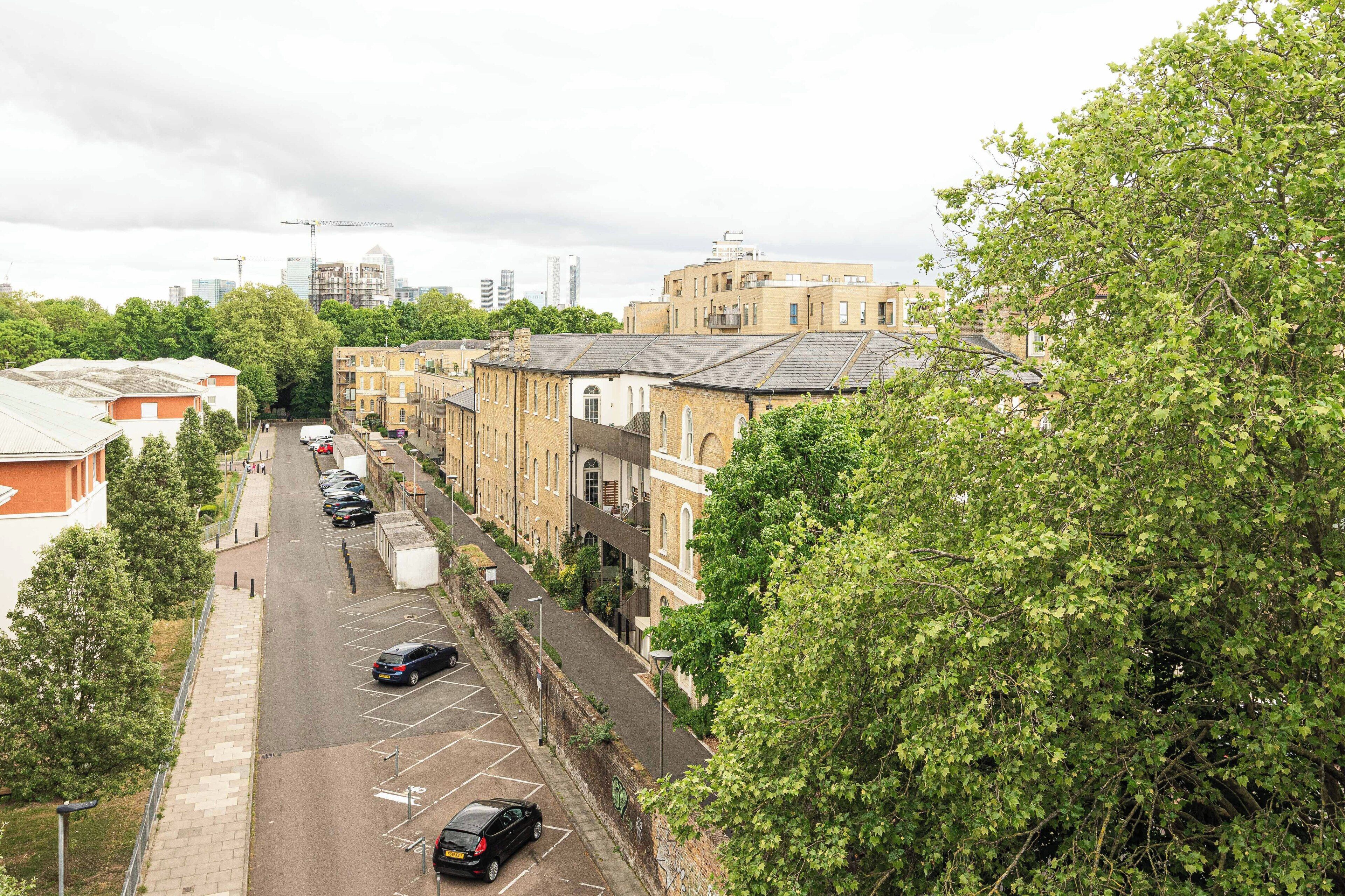 A street view with parked cars, buildings, and trees.