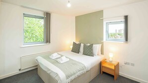 Un dormitorio ordenado con cama, mesitas de noche y dos ventanas.