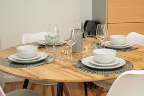 A round wooden dining table set with white plates, bowls, and wine glasses, surrounded by white chairs. - Clean & Comfortable 2-Bed with Views in Mile End (London)