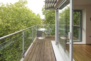 Un balcon avec une porte vitrée, une terrasse en bois et une table avec des chaises.