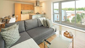 Una sala de estar moderna con un sofá gris, una mesa de centro de vidrio y vistas a la ciudad a través de amplios ventanales.
