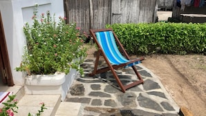 A wooden chair with a blue and white striped cushion, a white planter with pink flowers, and a stone-paved area. - CASA DENISE ILE SAINTE MARIE VOHILAVA MADA New fully-equipped house with garden (sainte marie - ambodifotatra)