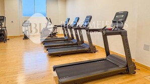 Une salle de sport équipée de plusieurs tapis de course, d’un vélo d’appartement et d’un appareil d’aviron.