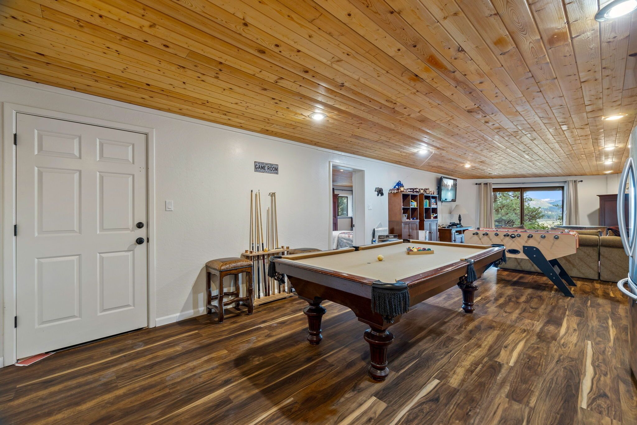 A game room with a pool table, billiard cues, and a foosball table.