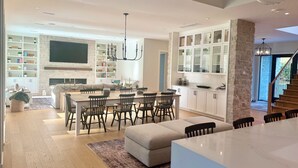A modern kitchen with white cabinetry, a central island, and a dining area with chairs and a table. - FIFA World Cup. Brand new 6 BD, 8 BA, Whiskey Room, Games room+ more (West Vancouver)